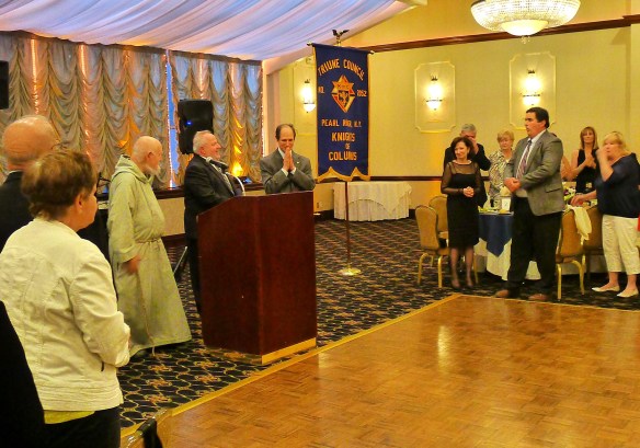 At the podium, Fr. Andrew Apostoli, CFR, Grand Knight John Rio, and Good Counsel Home's Chris Bell at the Triune Council #2052 96th Anniversary Charity Ball.